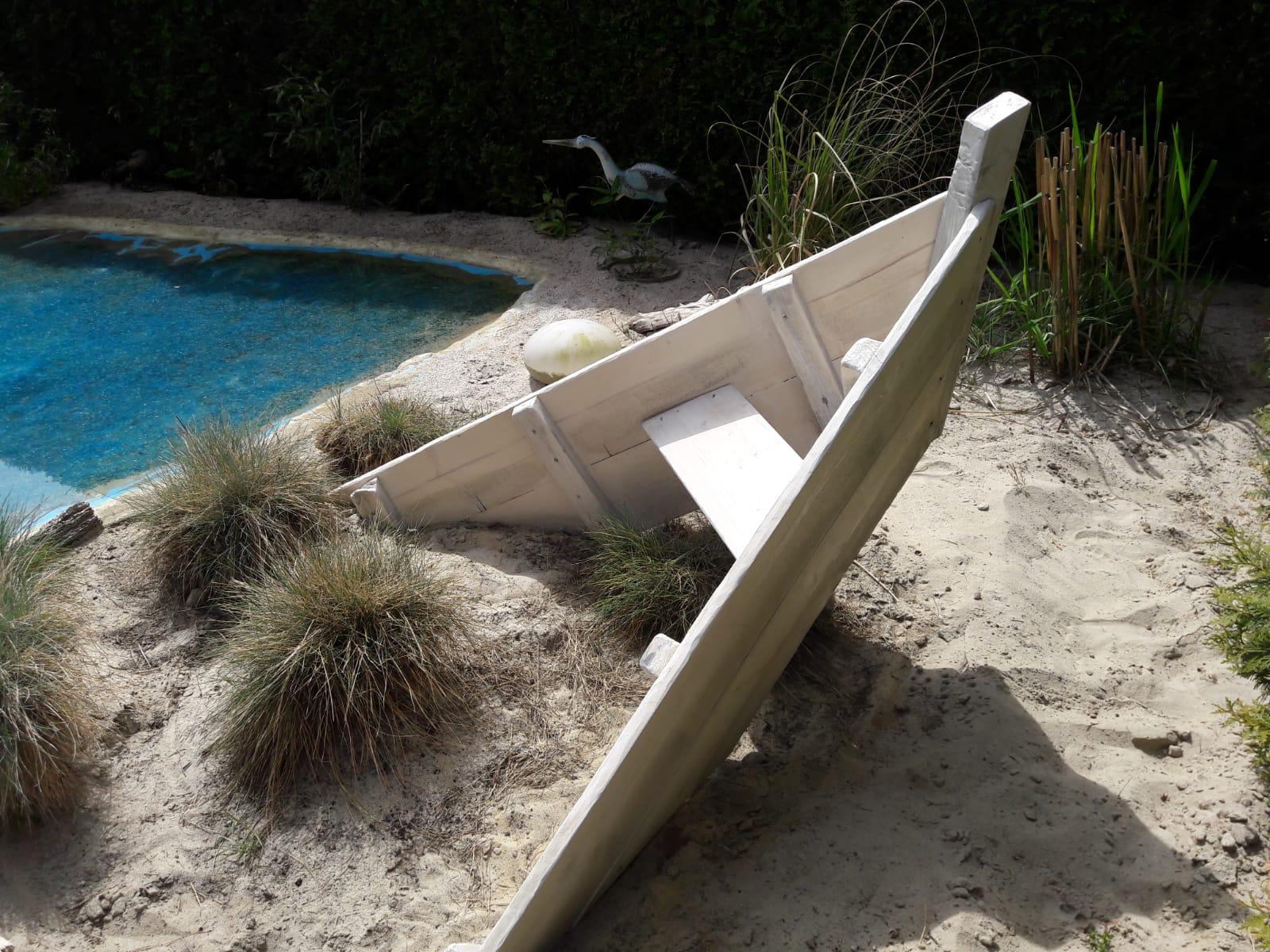 Ein Holzboot liegt im Sand, direkt neben einem Teich.